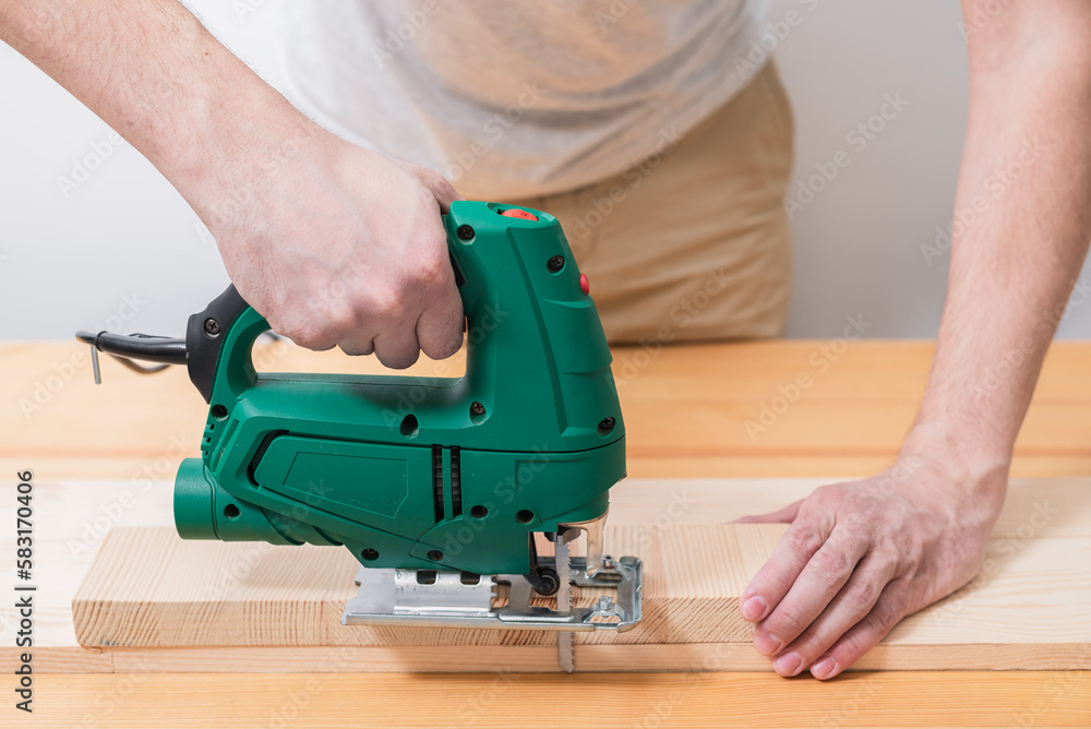 A man works with an electric jigsaw for wood on a wooden table with and without gloves and measures with a tape measure