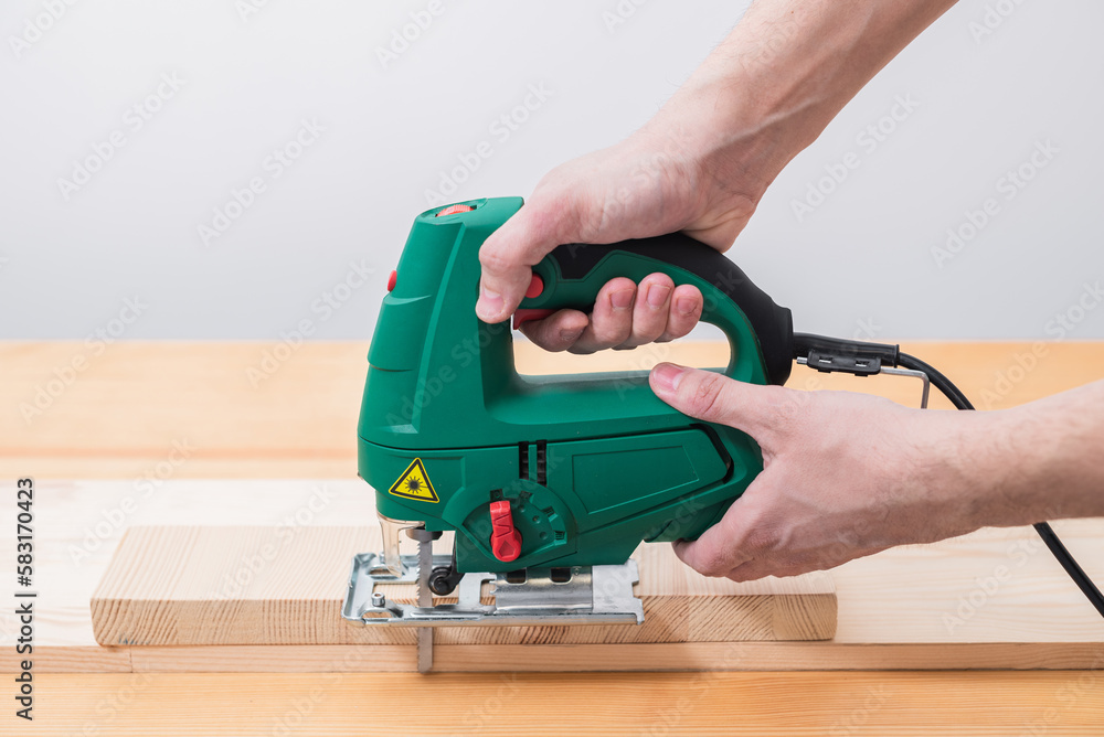 A man works with an electric jigsaw for wood on a wooden table with and without gloves and measures with a tape measure