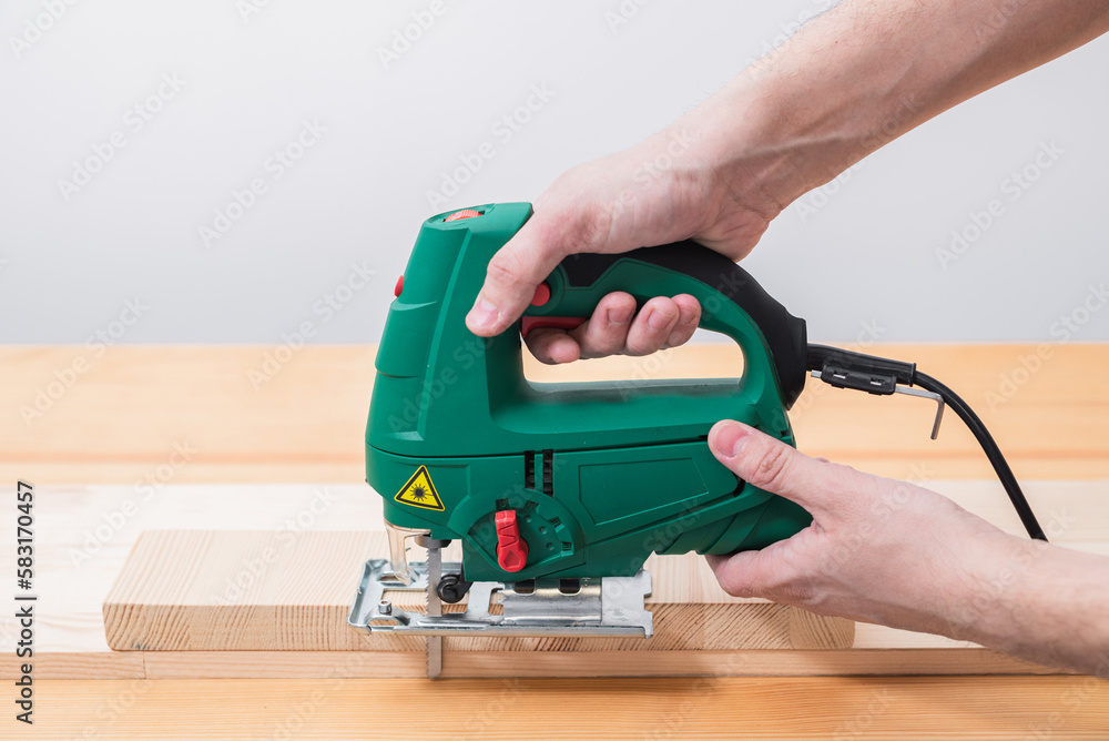 A man works with an electric jigsaw for wood on a wooden table with and without gloves and measures with a tape measure A man works with an electric jigsaw for wood on a wooden table with and without gloves and measures with a tape measure