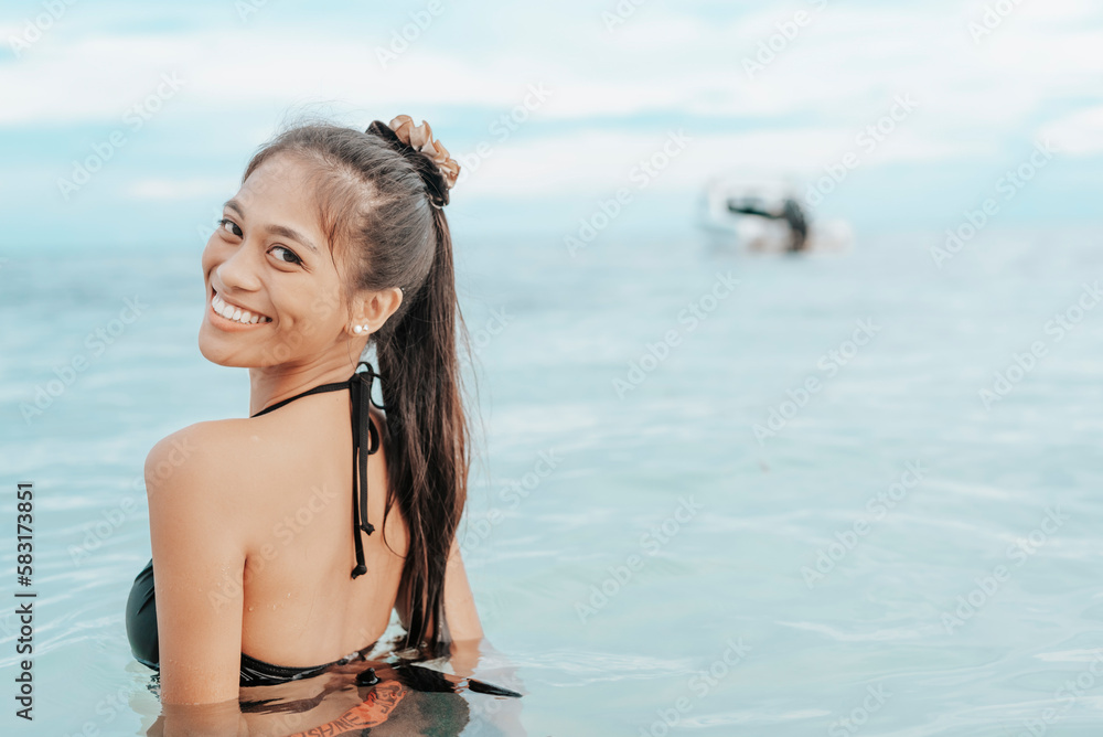 A young slim asian woman enjoying a dip at the beach. A female tourist unwinding in chest deep waters. Vacation scene.