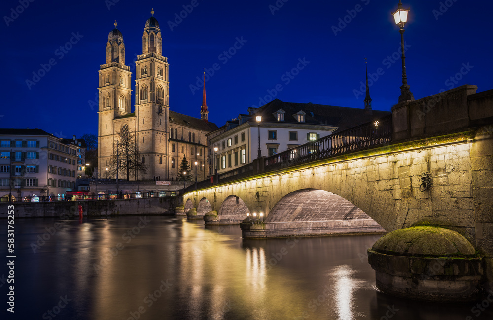 Panorama of Grossmünster church and bridge in Zürich city center during evening with street lights