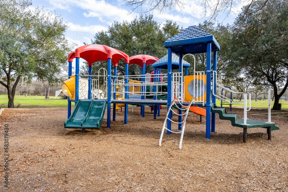 Colorful children's playground activities in a public park surrounded by trees in the daytime Colorful children's playground activities in a public park surrounded by trees in the daytime