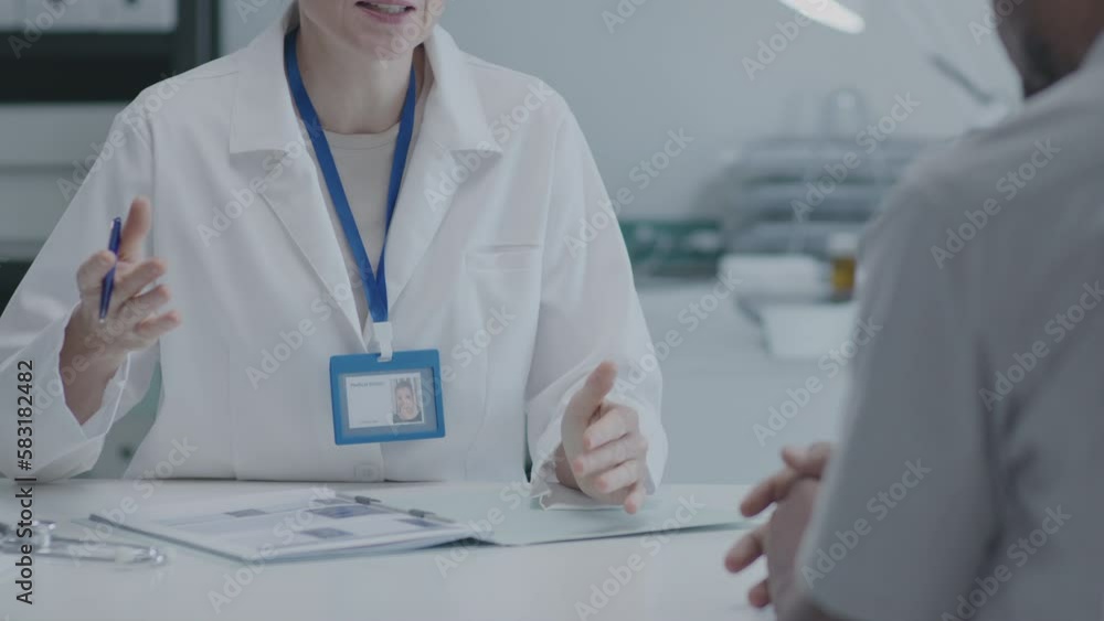 Female general practitioner sitting behind the table speaking to patient at the consultation in medical center. Zoom out shot Female general practitioner sitting behind the table speaking to patient at the consultation in medical center. Zoom out shot
