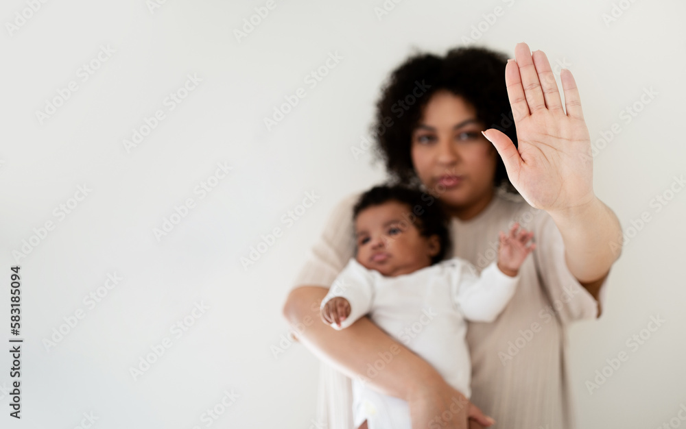 Serious confident young african american lady hold baby in arms, making stop gesture with hand Serious confident young african american lady hold baby in arms, making stop gesture with hand