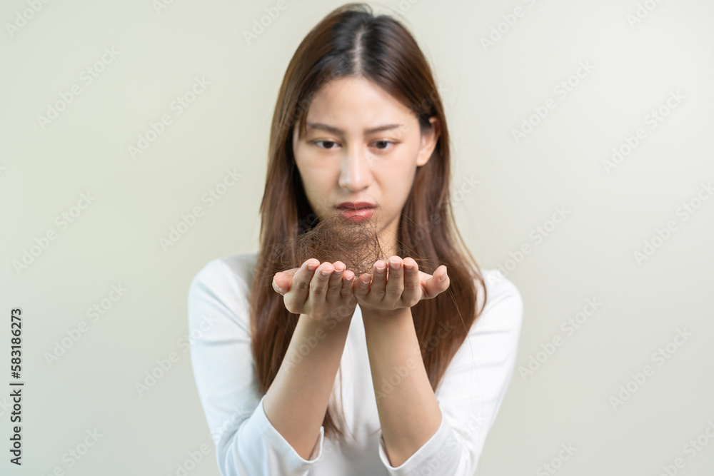Serious, worried asian young woman, girl holding, show damaged loss hair, problem after brushing, hair fall out on her hand in living room at home isolated on background. Health care, beauty treatment Serious, worried asian young woman, girl holding, show damaged loss hair, problem after brushing, hair fall out on her hand in living room at home isolated on background. Health care, beauty treatment