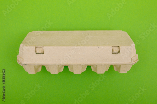 Closed egg box with ten eggs. Close carton pack or egg container top view with copy space. Egg box with chicken eggs, carton pack or egg container. Green background.