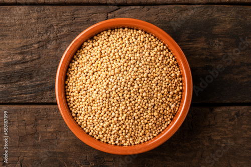 Mustard seeds in bowl on retro wooden background. Top view
