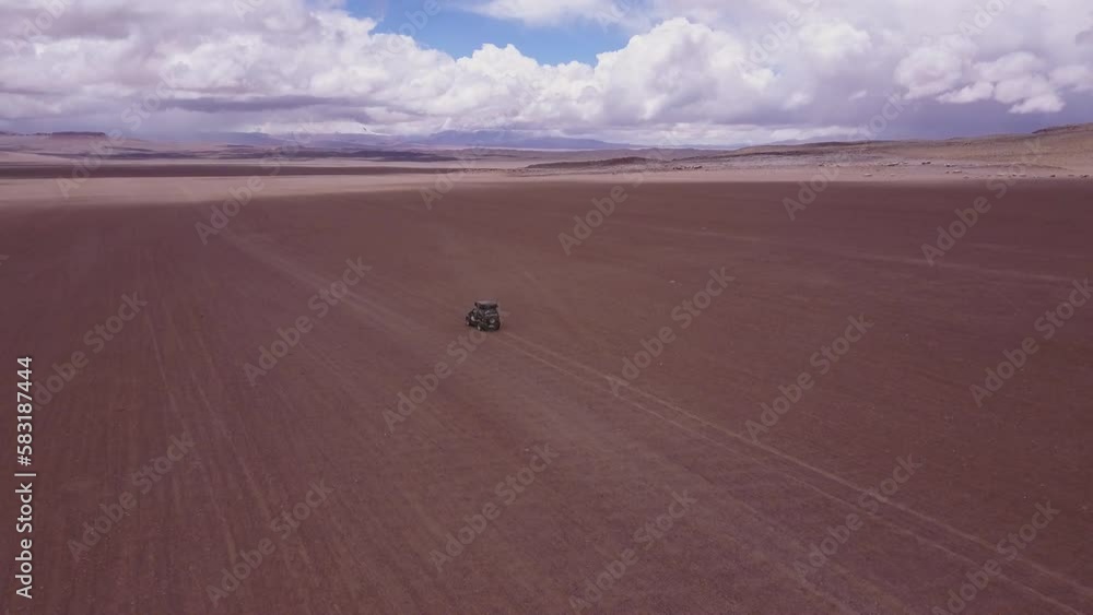 Drone view of a car driving across a desert under a blue cloudy sky and sunlight in Bolivia Drone view of a car driving across a desert under a blue cloudy sky and sunlight in Bolivia