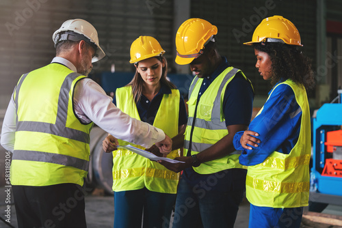 Group of diverse warehouse worker in safety suit, Project manager using blueprint and digital tablet to discussing with engineer team for work in construction industry. Teamwork and unity concept.