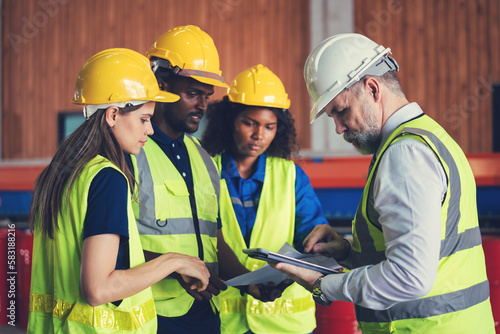 Group of diverse warehouse worker in safety suit, Project manager using blueprint and digital tablet to discussing with engineer team for work in construction industry. Teamwork and unity concept.