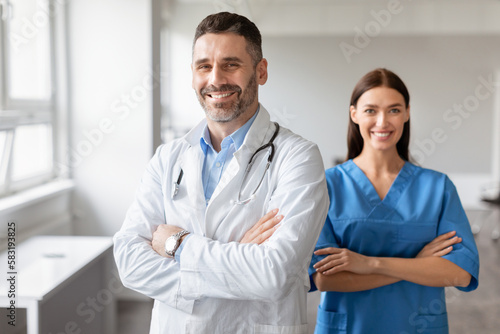 Happy male doctor and female nurse colleagues  wearing coats  standing with folded arms  posing at medical office