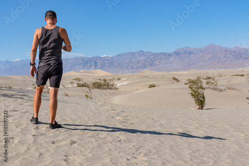 Rear view of man looking at Mesquite Flat Sand Dunes in Death Valley National Park, California, USA. Panoramic view on dry Mojave desert on sunny summer day with Amargosa Mountain Range in the back