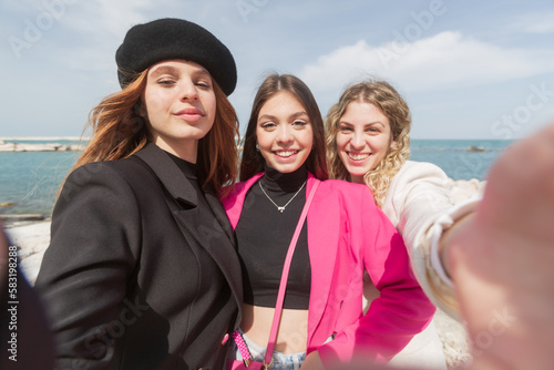 Three beautiful girls pose outdoors against the sky, the brunette with the black hat and the blonde with curly hair and a very young brunette with long hair