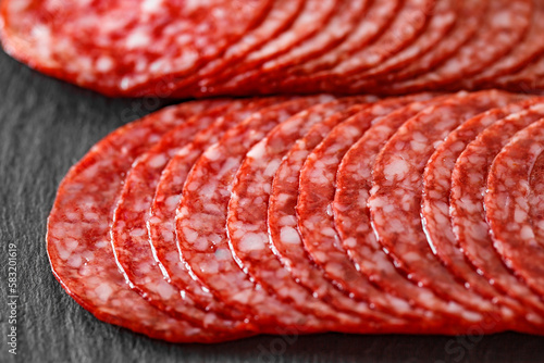 Salami sausage meat with bacon cut into circles in two rows close-up on slate stone plate, dark background, side view, selective focus. © elenvd