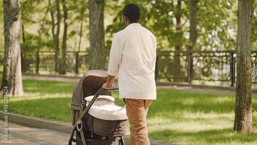 Young man walking with baby stroller in park, paternal leave, family