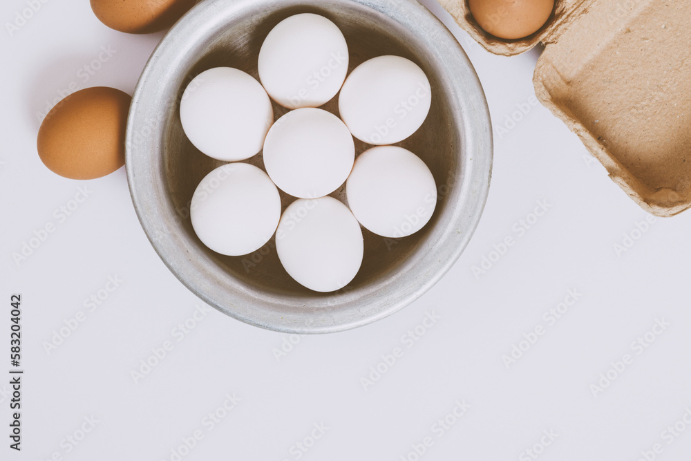 Brown eggs on bright background. White eggs in metal bowl and eggs in brown tray on bright background. Close up, selective focus. Concept scene. Top view. Brown eggs on bright background. White eggs in metal bowl and eggs in brown tray on bright background. Close up, selective focus. Concept scene. Top view.