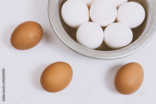 Brown eggs on bright background and white eggs in metal bowl. Close up, selective focus. Concept scene. 