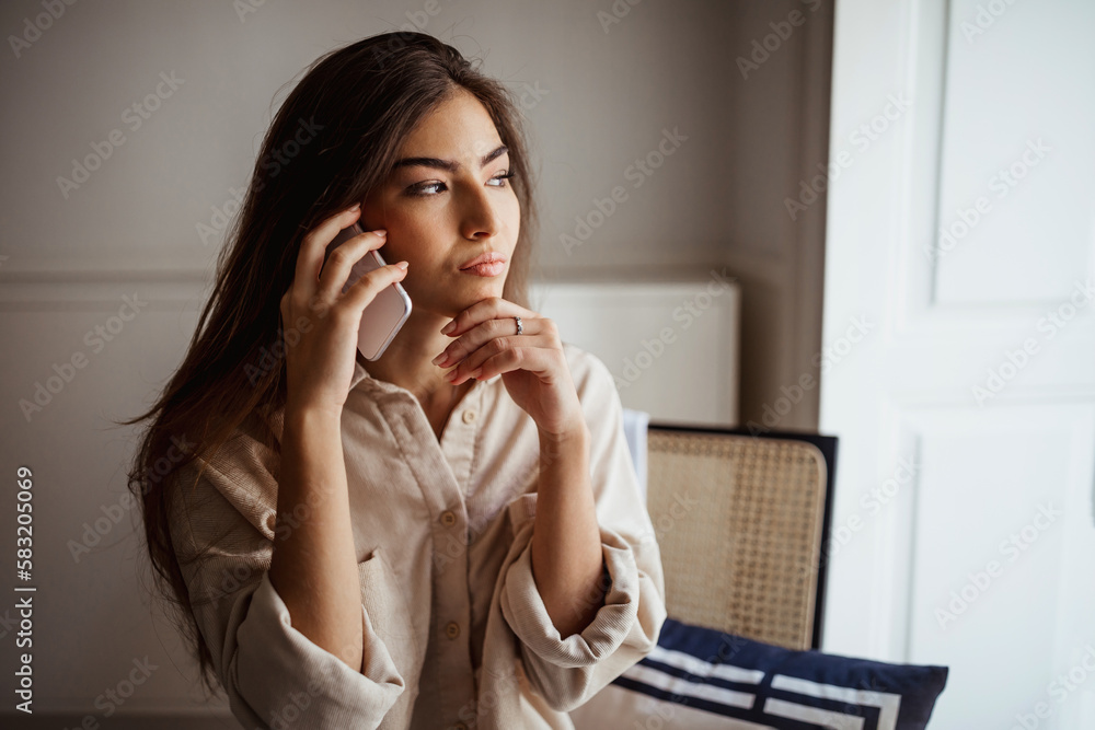 Thoughtful serious millennial mixed race lady calls by smartphone, talks, thinks, sits on chair Thoughtful serious millennial mixed race lady calls by smartphone, talks, thinks, sits on chair