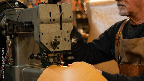 Photography closeup of leather craftsman while sewing sitting in his workshop in the histori