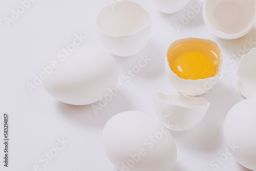 Whole white chicken eggs and cracked egg half with a yolk inside on bright background. Selective focus.