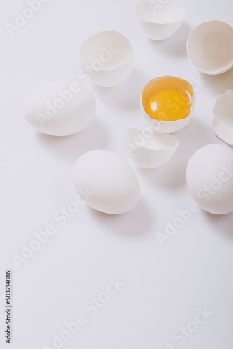 Whole white chicken eggs and cracked egg half with a yolk inside on bright background. Selective focus.