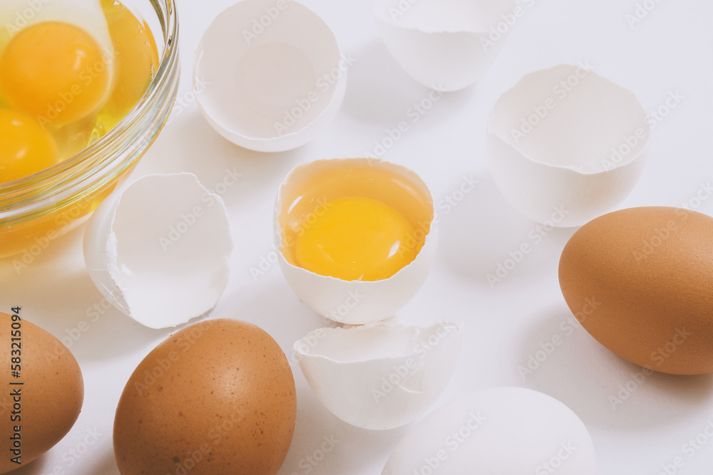 Whole brown eggs and cracked white eggs half with a yolk inside near the glass bowl with egg yolks and egg whites on bright background. Close up, selective focus. Whole brown eggs and cracked white eggs half with a yolk inside near the glass bowl with egg yolks and egg whites on bright background. Close up, selective focus.