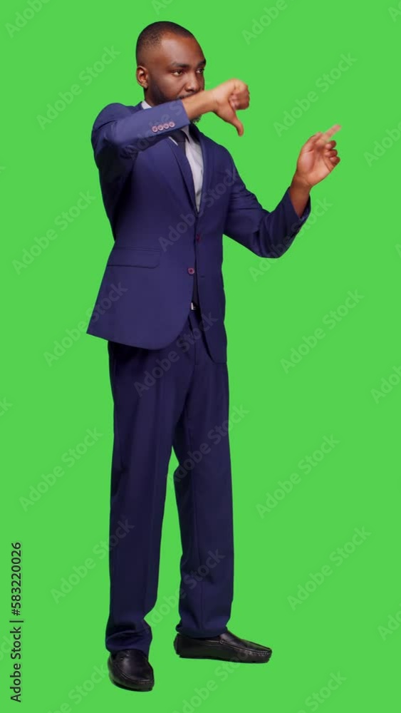 Vertical video: Side view of negative office worker doing thumbs down in studio, wearing formal suit over greenscreen background. Young businessman showing dislike gesture and expressing disapproval Vertical video: Side view of negative office worker doing thumbs down in studio, wearing formal suit over greenscreen background. Young businessman showing dislike gesture and expressing disapproval