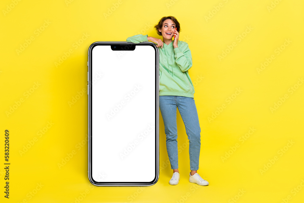 Full length photo of pretty dreamy girl dressed green sweatshirt communicating modern device empty space isolated yellow color background Full length photo of pretty dreamy girl dressed green sweatshirt communicating modern device empty space isolated yellow color background