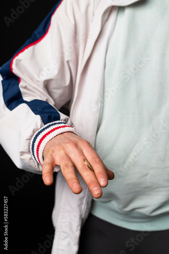 Close-up of a Street guy dressed in a tracksuit flipping a coin between his fingers. Urban street culture, street gang.