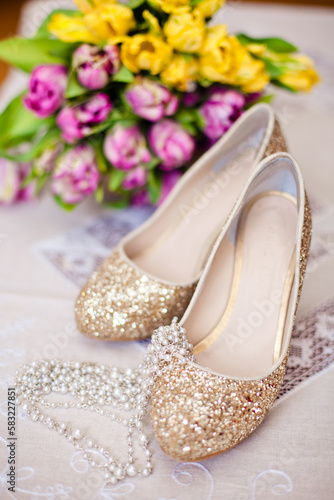 Shoes with gold glitter against a backdrop of yellow and pink tulips along with beads