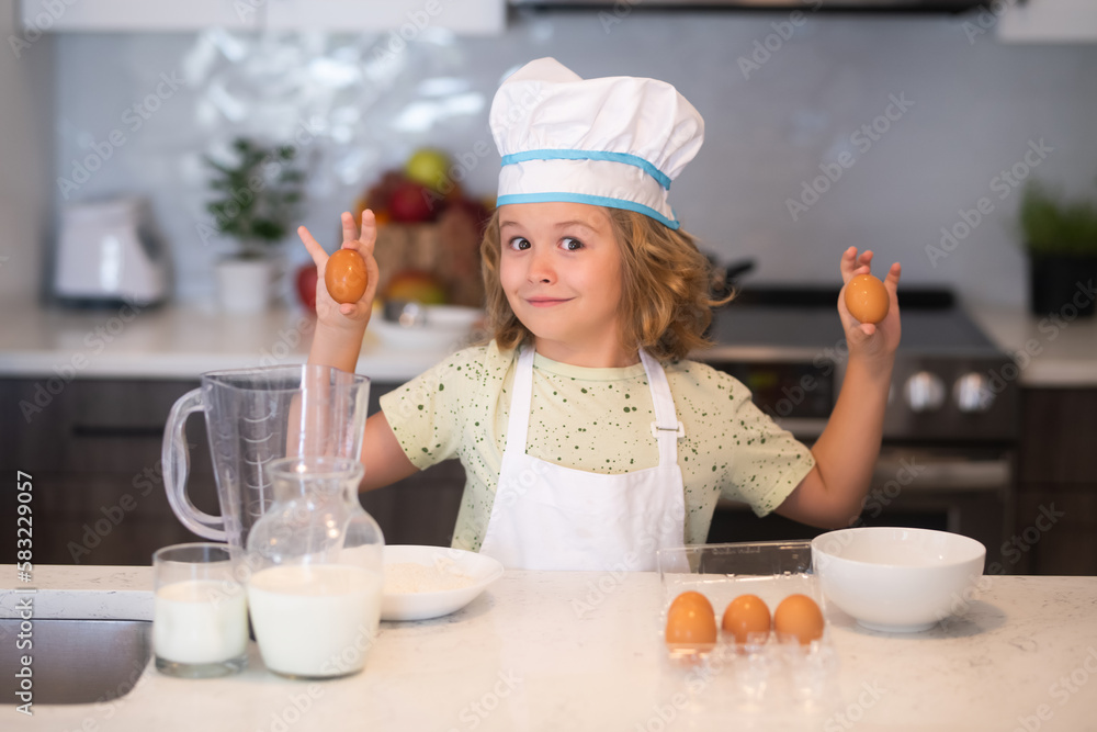 Kid chef cook with eggs at kitchen. Kid chef cook wearing cooker uniform and chef hat preparing food on kitchen. Cooking, culinary and kids food concept. Kid chef cook with eggs at kitchen. Kid chef cook wearing cooker uniform and chef hat preparing food on kitchen. Cooking, culinary and kids food concept.