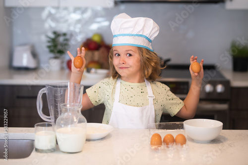 Kid chef cook with eggs at kitchen. Kid chef cook wearing cooker uniform and chef hat preparing food on kitchen. Cooking, culinary and kids food concept.