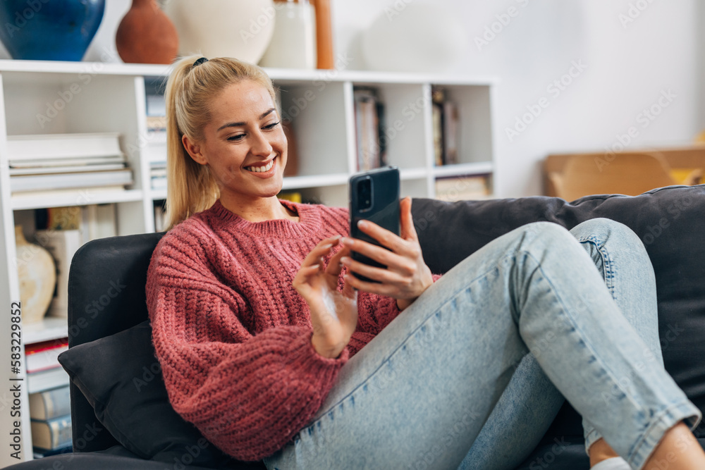 Obraz premium young adult caucasian woman sit on sofa and using smartphone
