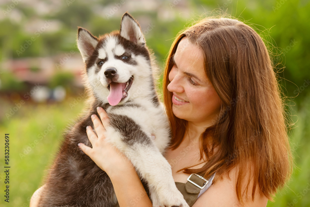 Woman playing with cute little husky puppy dog outdoors. Pet and owner love