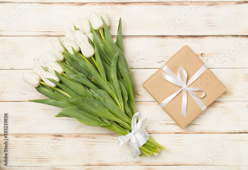 White tulip bouquet with gift box on wooden background, top view