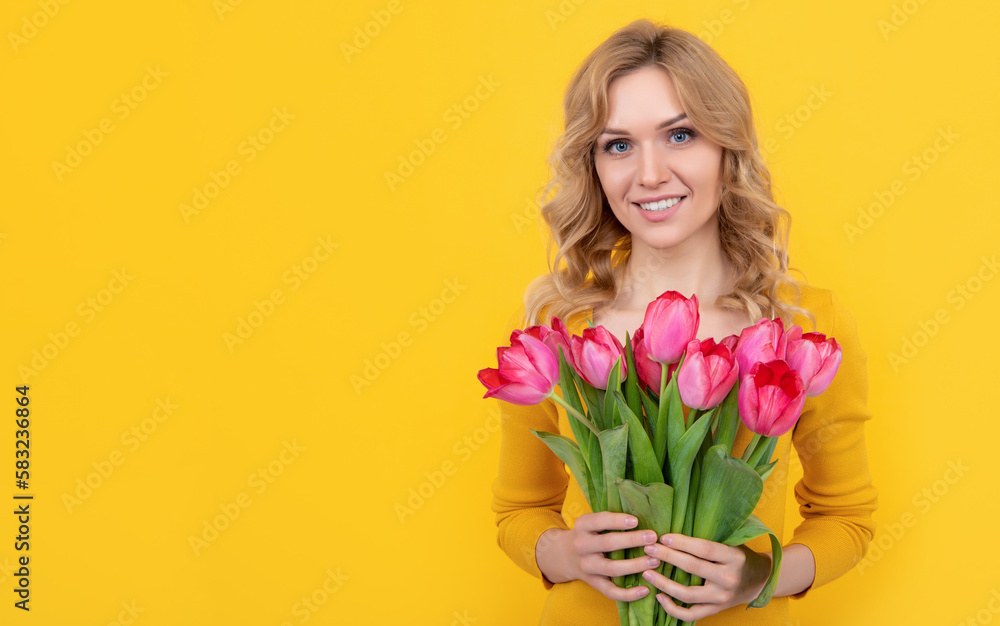 happy young blonde woman with spring tulip flowers on yellow background
