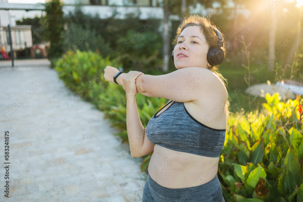 Young pretty smiling plus size woman in sporty top and leggings doing sport fitness and listen to music with headphones in summer morning outdoor copy space Young pretty smiling plus size woman in sporty top and leggings doing sport fitness and listen to music with headphones in summer morning outdoor copy space