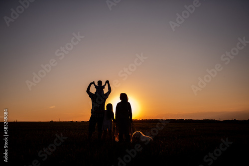 Silhouette of family with Samoyed dog at sunset. Faceless, people standing with backs to camera.