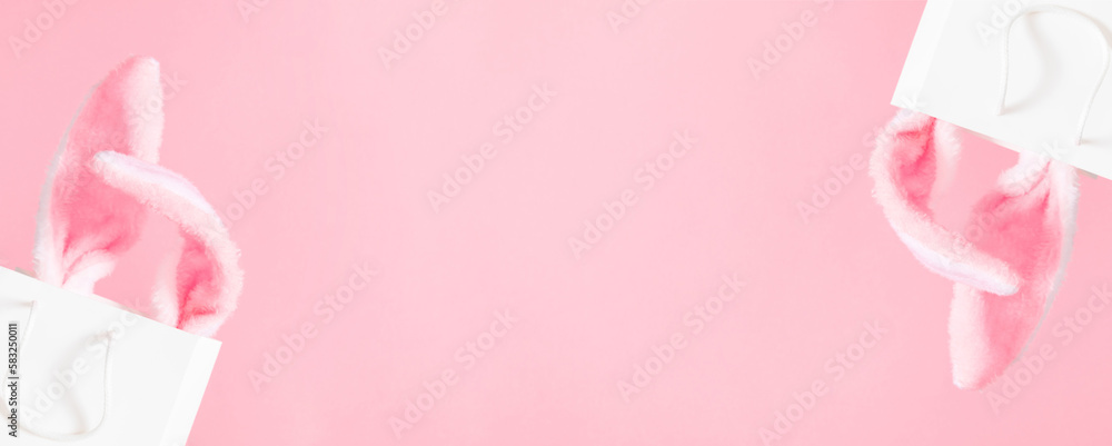 Easter market background, banner. Gift bag with bunny on pink table background. Top view of fluffy easter bunny ears. Concept of online shopping for Easter. Flat lay, top view, copy space