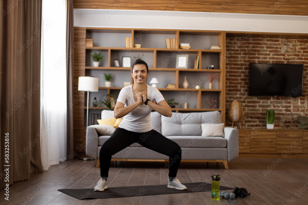 Young female athlete in activewear doing squats during home workout. Happy african brunette enjoying morning exercise. Sport, fitness and healthy lifestyle concept. Young female athlete in activewear doing squats during home workout. Happy african brunette enjoying morning exercise. Sport, fitness and healthy lifestyle concept.