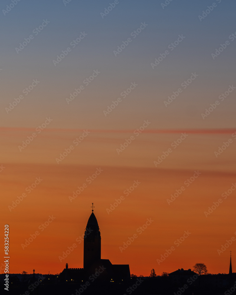 The majestic Masthugget Church stands silhouetted against a vivid orange sky at dawn, its stunning architecture the perfect backdrop to Gothenburgs skyline.