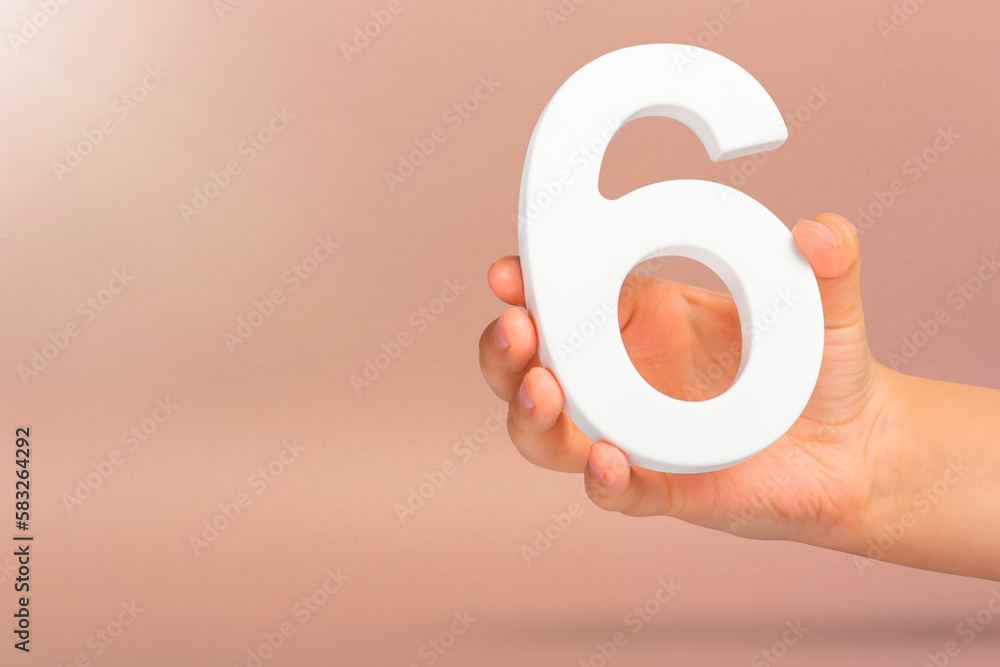 Number six in hand. A hand holds a white number 6 on a red background