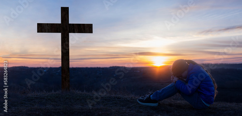 The girl kneels and prays. Man worships before God Jesus. Prayer to Christ. Crucifix on the background of the mountain. Repentance on the knees.