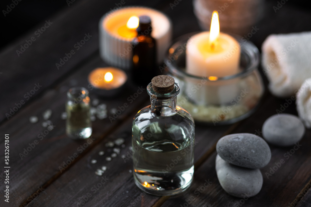 Spa setting with essential oil, candle, sea salt, pebbles, towel on dark wooden background. Massage, aromatherapy. Natural organic ingredients for relaxation, detention. Wellness in salon concept Spa setting with essential oil, candle, sea salt, pebbles, towel on dark wooden background. Massage, aromatherapy. Natural organic ingredients for relaxation, detention. Wellness in salon concept