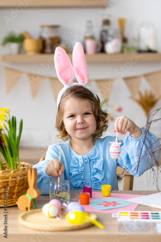 Photography Portrait of cute pretty little girl in blue dress and funny rabbit ears making craft, diy eggs for easter holiday home decoration