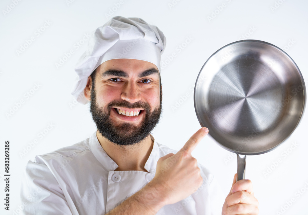 Young male chef showing a stainless pan while smiling and looking at camera. Isolated on a white background Young male chef showing a stainless pan while smiling and looking at camera. Isolated on a white background