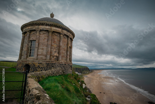 Mussenden temple in northern ireland at demesne downhill on a cloudy day hiding between the grass. Beautiful mausoleum in irish countryside.