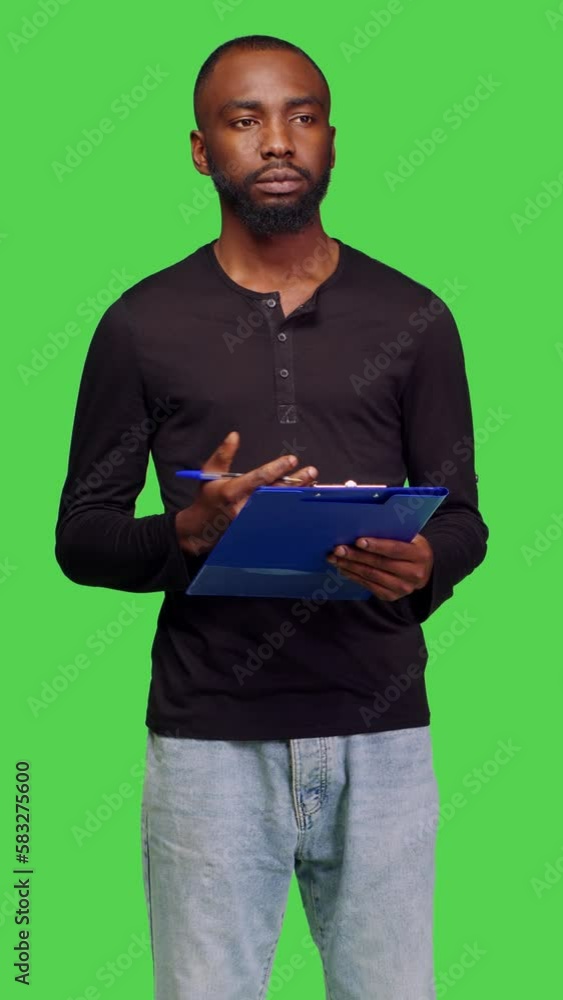 Vertical video: Front view of casual person taking notes on papers over greenscreen backdrop, writing information on files with clipboard. Young model brainstorming new ideas in studio, professional Vertical video: Front view of casual person taking notes on papers over greenscreen backdrop, writing information on files with clipboard. Young model brainstorming new ideas in studio, professional
