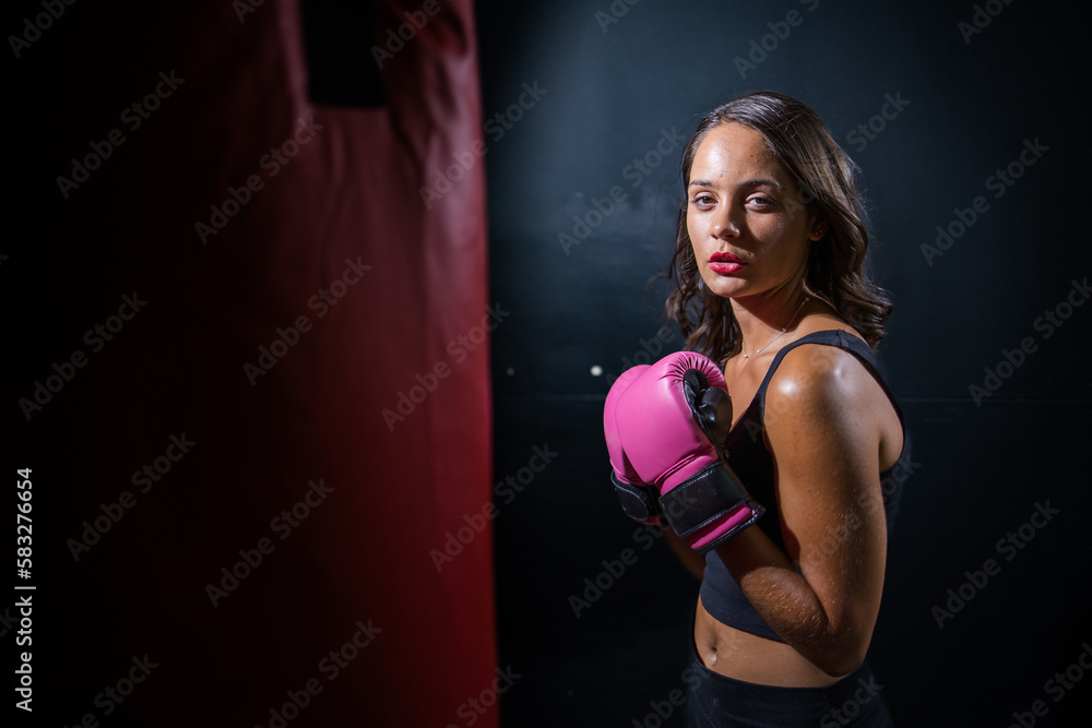 Dark Haired Girl Boxing a Punching Bag in a Moody Setting Dark Haired Girl Boxing a Punching Bag in a Moody Setting
