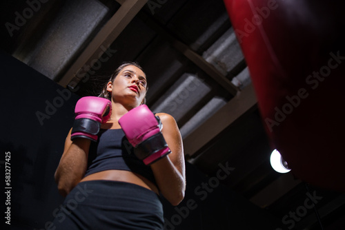 Dark Haired Girl Boxing a Punching Bag in a Moody Setting © Dewald